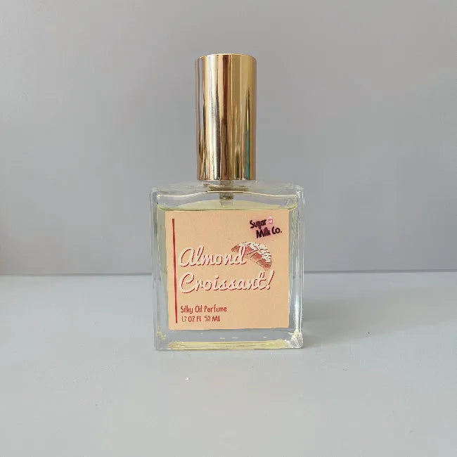 Perfume bottle with gold cap and 'Almond Croissant' label on a gray background from Sugar Milk Co
