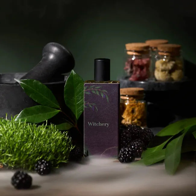Perfume bottle from Sorce labeled 'Witchery' with blackberries, green leaves, and jars in the background.